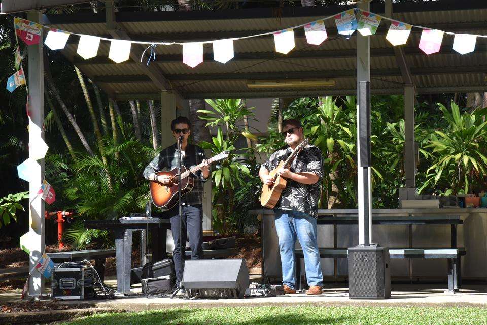 Two musicians play near a barbecue setting with end loneliness flags above.jpg