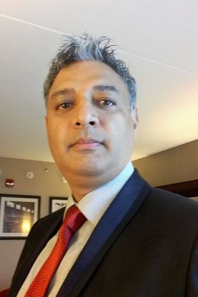 Robin Amatya smiling with black suit, white shirt and red tie in hotel foyer