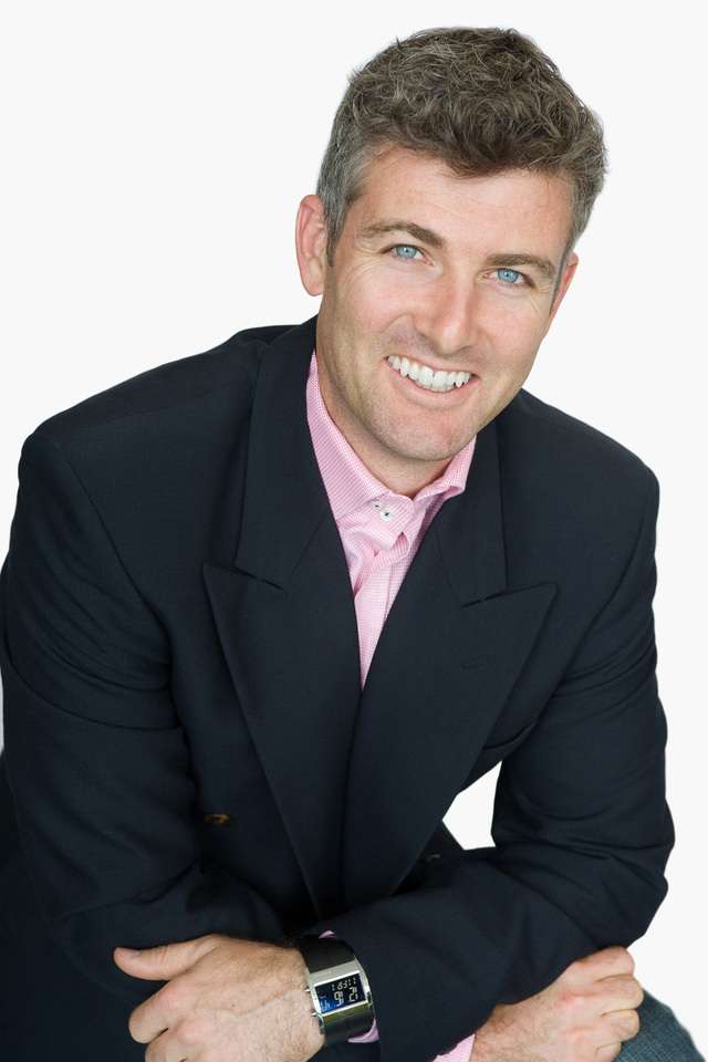 Jason Titman smiling with arms crossed whilst wearing black suit coat and pink business shirt