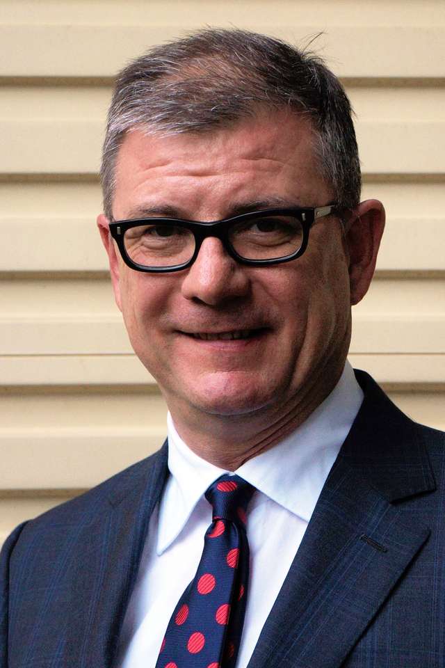Sandy Horneman-Wren smiling with black reading glasses and navy suit with blue tie with red circles