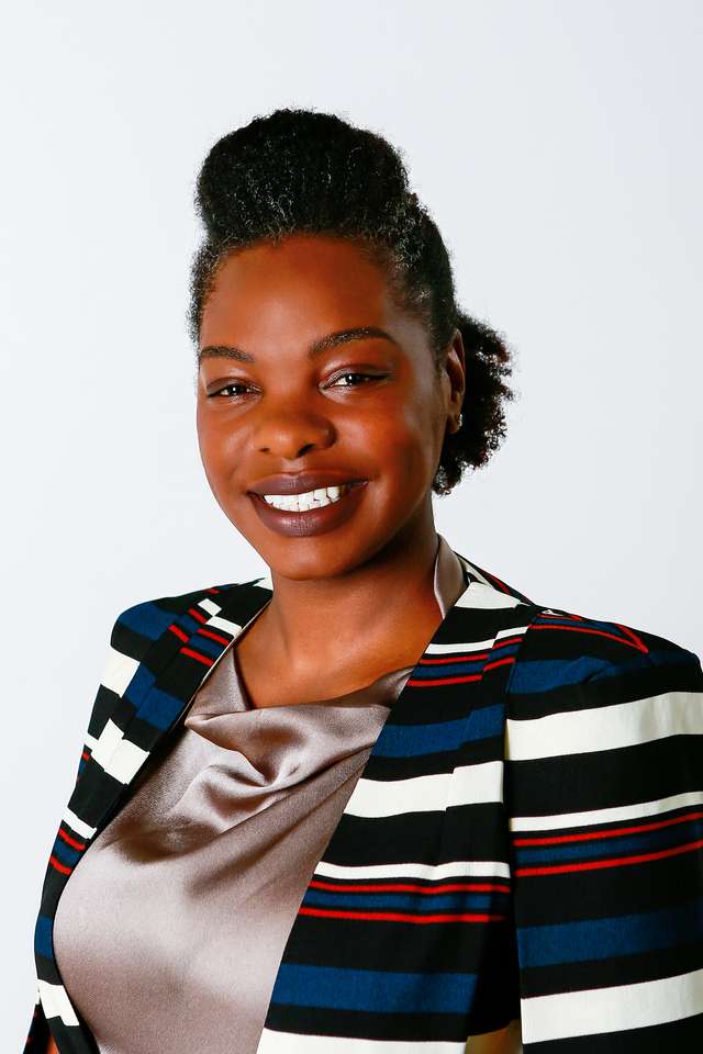 Tandi Kuwana smiling wearing light pink dress and brightly coloured suit coat