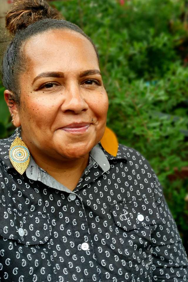 Dr Melinda Mann smiling with First Nations artwork designed teardrop earrings