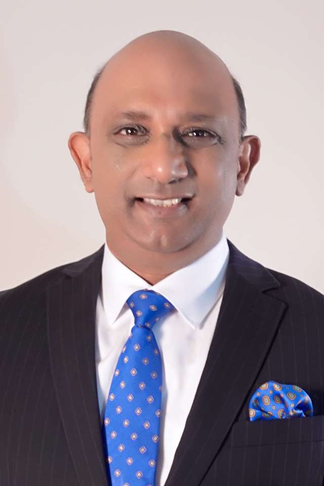 Kumar Parakala smiling wearing black suit and white business shirt with bright blue tie