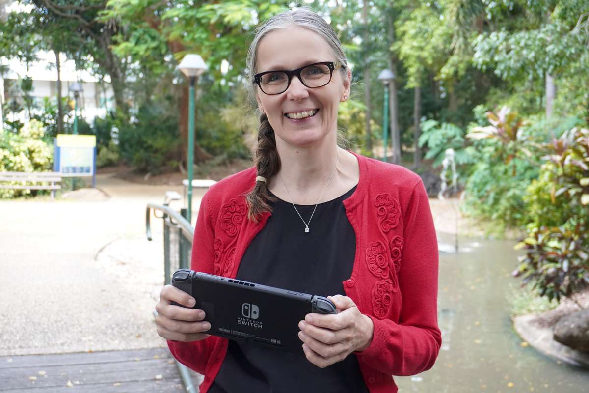 CQU academic Dr Fae Heaselgrave stands outdoors holding a Nintendo Switch device.