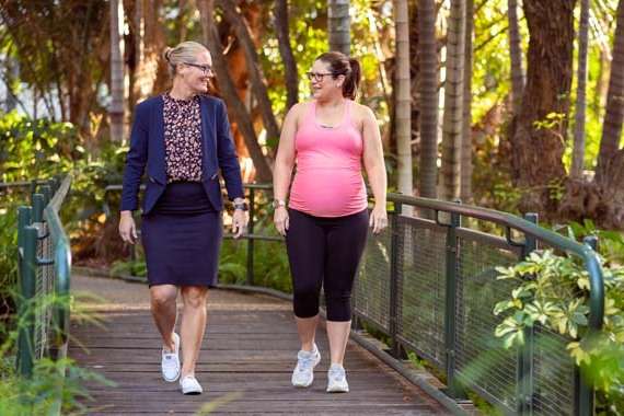 A pregnant woman walking in a park with a friend