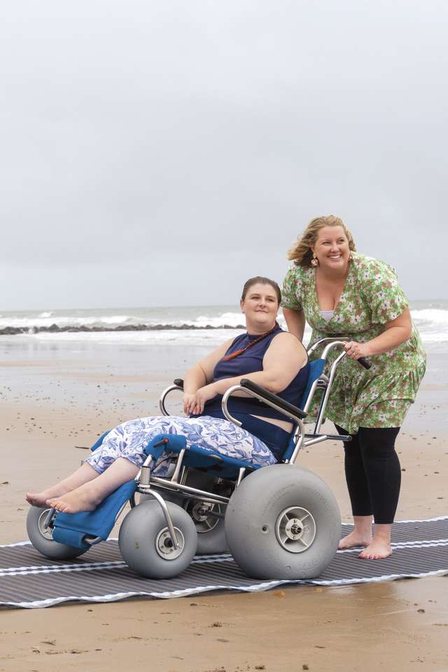 Student helping another student in a wheelchair down the beach smiling at the ocean.