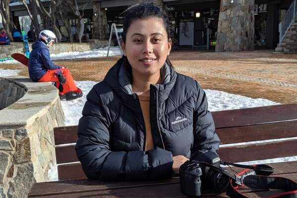 Anita Thapa smiling in a snowy outside area with a camera on the table in front of her