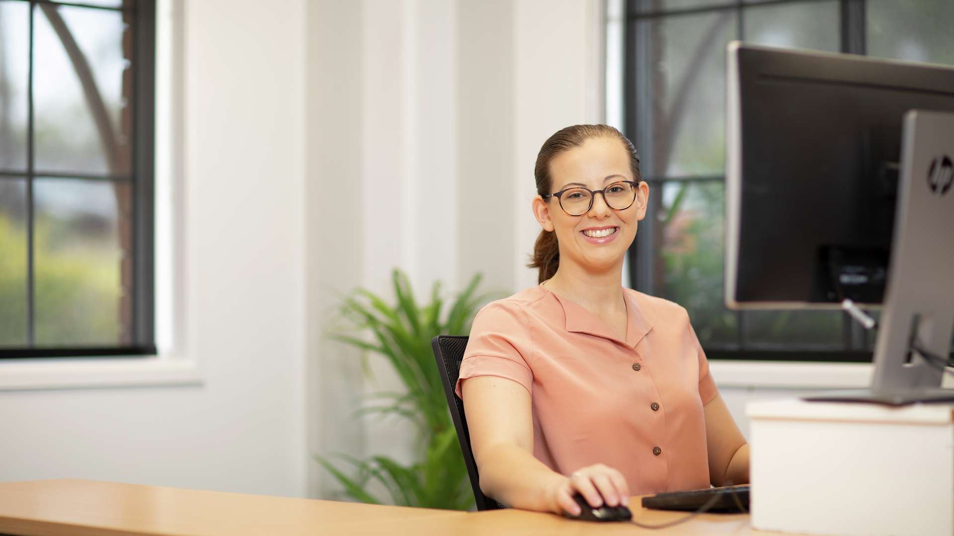 Person sitting at a desk, with a computer, smiling at camera