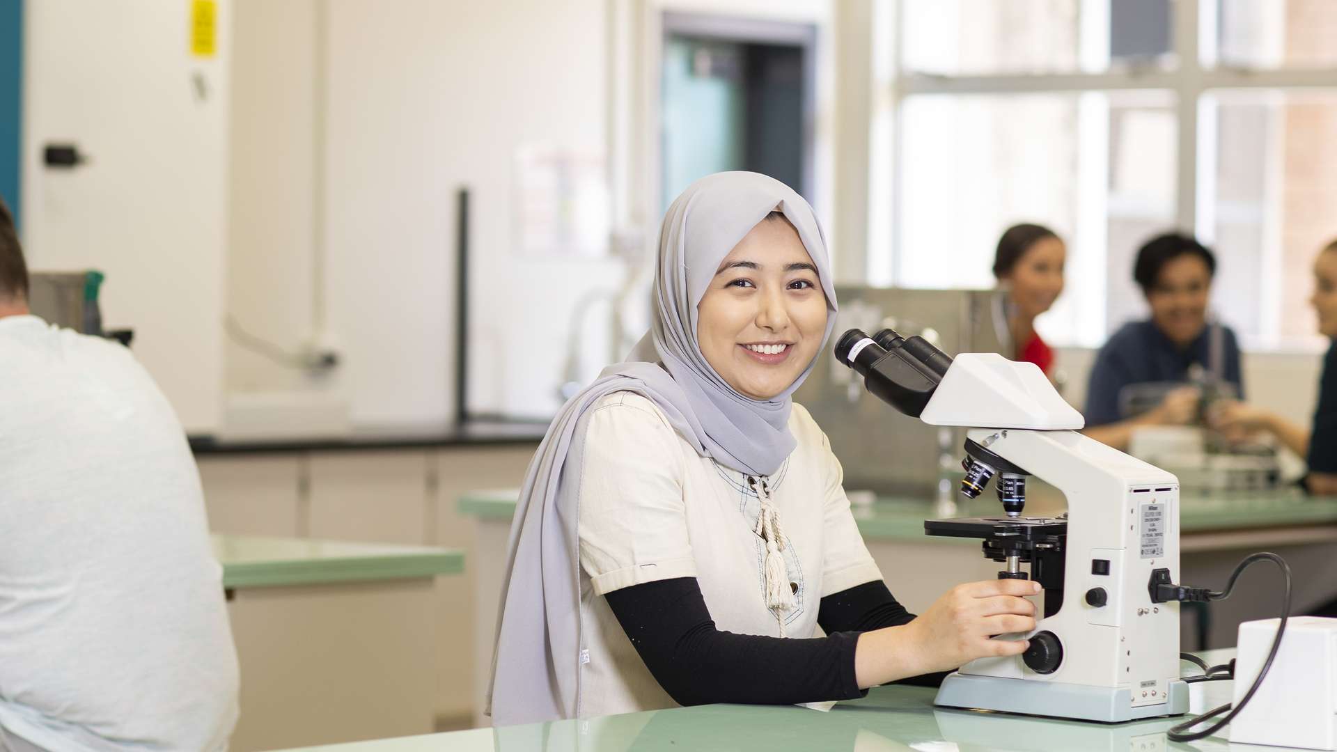 Medical students working in a laboratory, with a student using a microscope in focus.