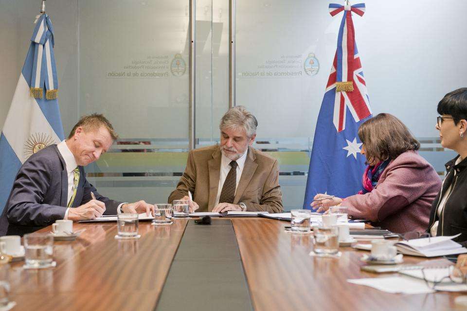 Professor Nick Klomp, Argentina’s Minister for Science and Technology Daniel Filmus and CONICET President Dr Ana Franchi sit at a boardroom table while signing a memorandum of understanding to create research linkages between the three organisations. The Argentine and Australian flags are positioned in the background.