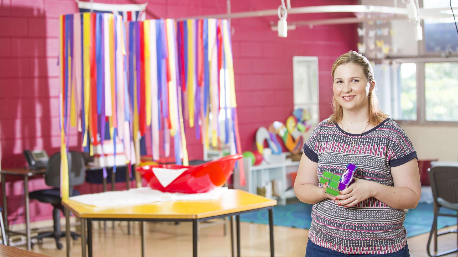 A student standing in front of the camera in a childcare room holding some blocks.