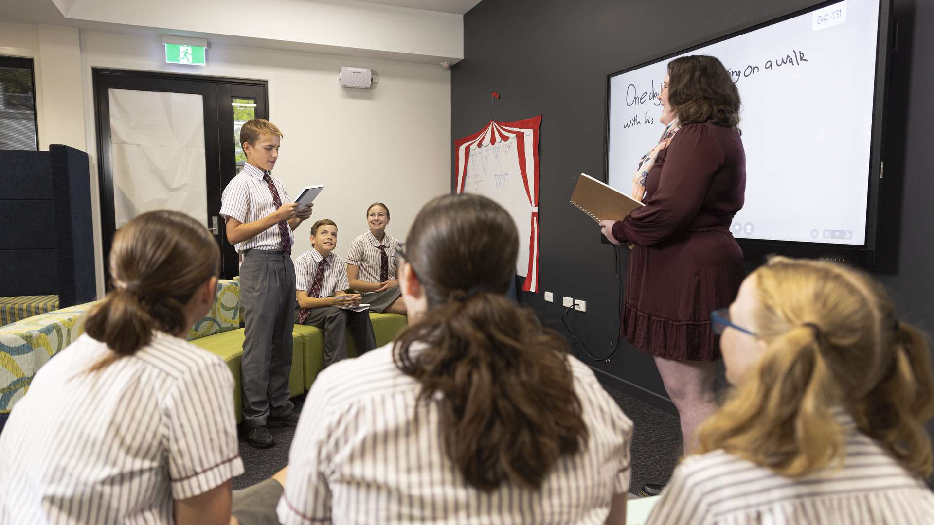 A teaching student listening to a school student present in front of the rest of the class.