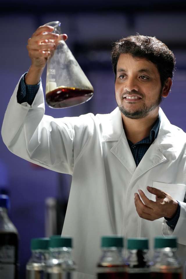 Engineering student with lab coat measuring chemicals.