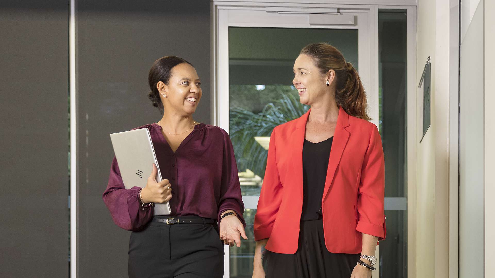 Two women, dressed professionally, walking down a hall talking with each other