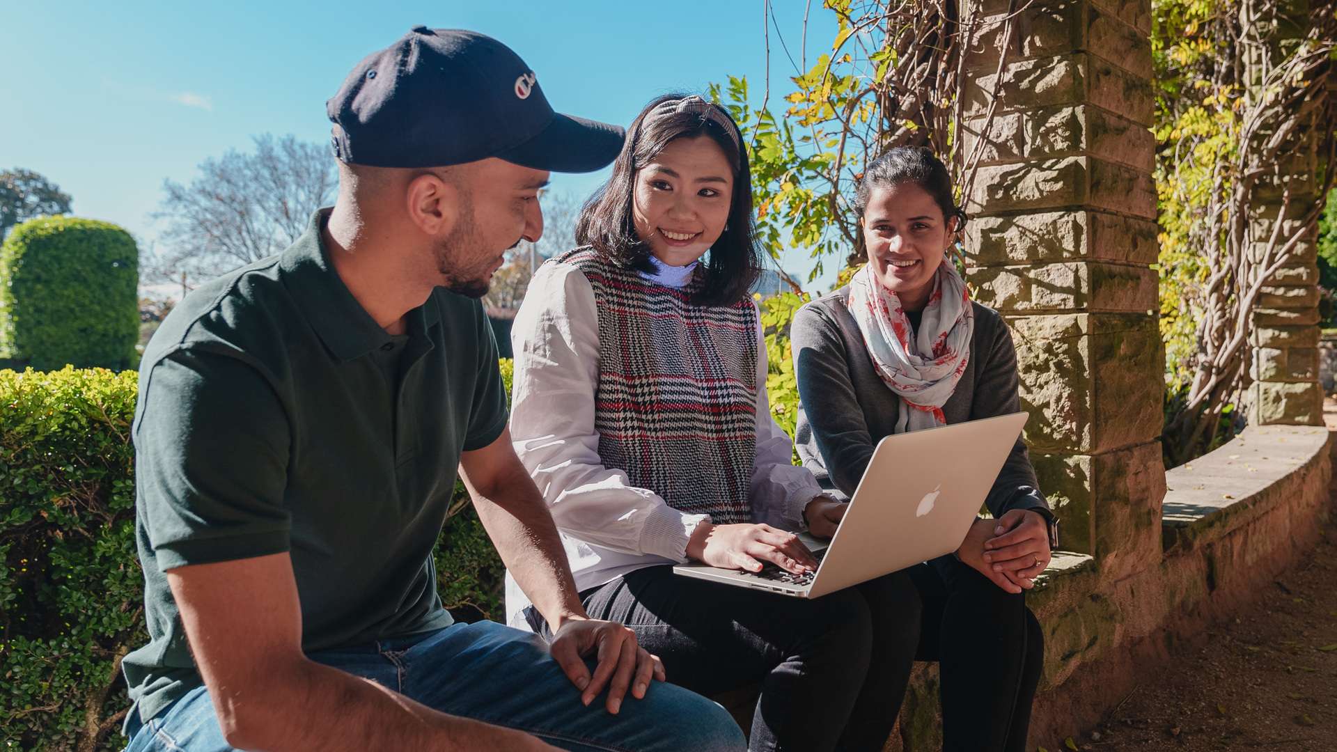 Three students chatting and using a laptop outside in Jakarta, Indonesia