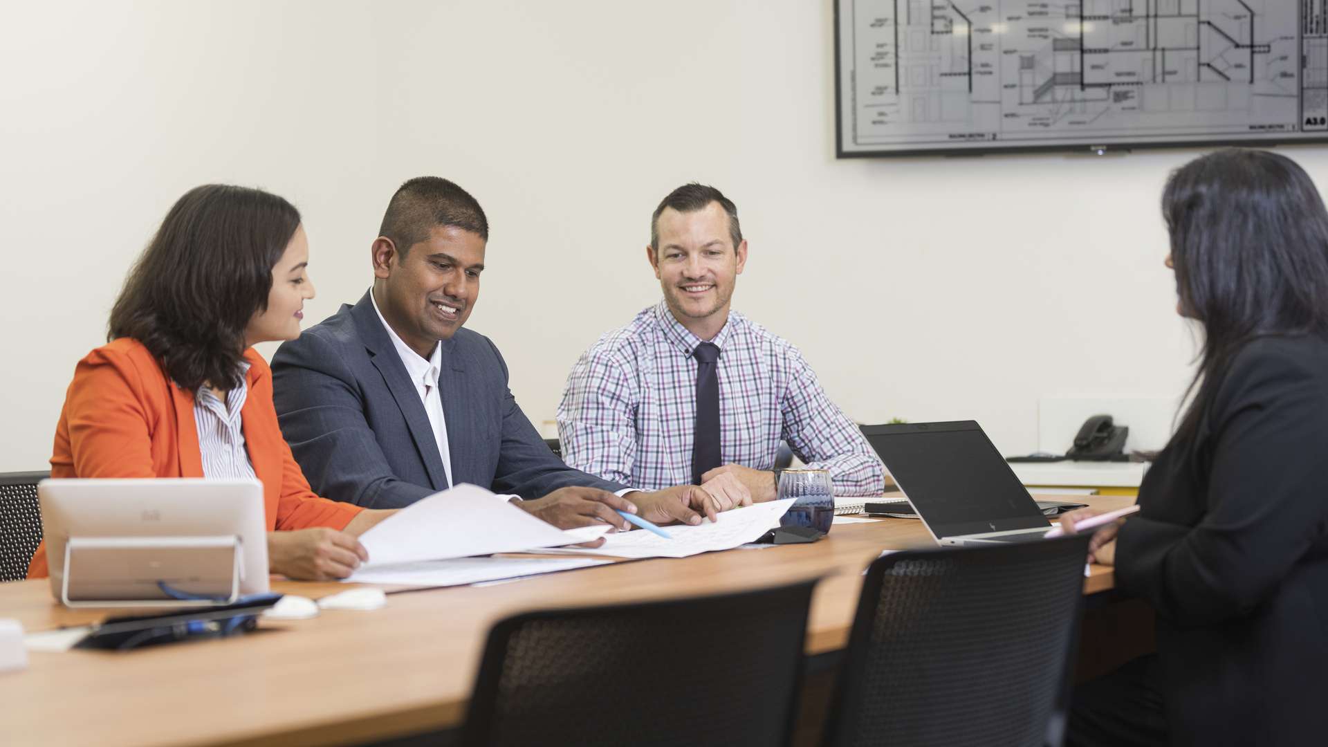 Construction students sitting down having a meeting. Construction plans are displayed on a screen in the background.