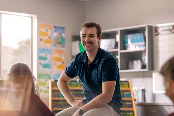 Male teacher sitting in classrooms smiling at students