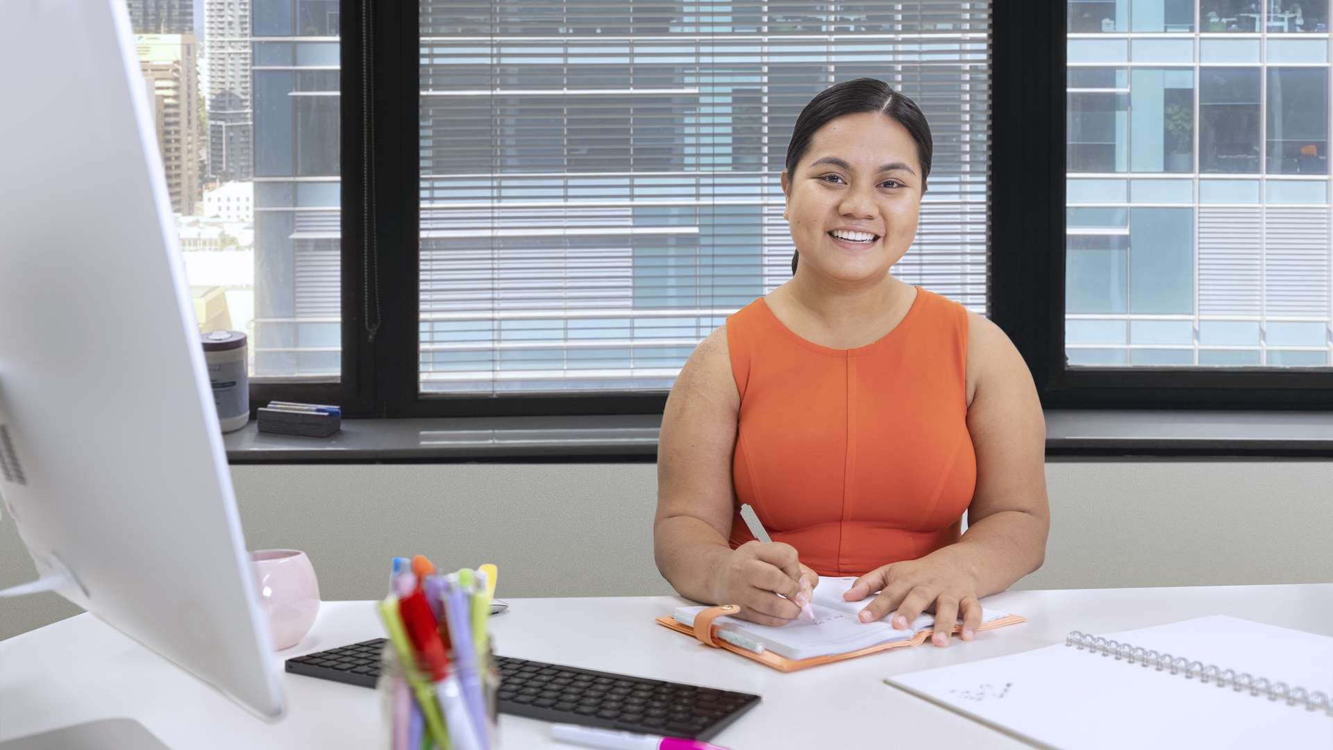 A business student studying at a desk in front of a computer, smiling at the camera.