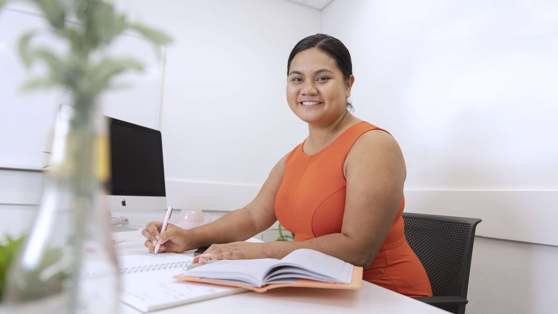 An Accounting student studying at a desk with a notepad and computer. A plant is out of focus in the foreground.