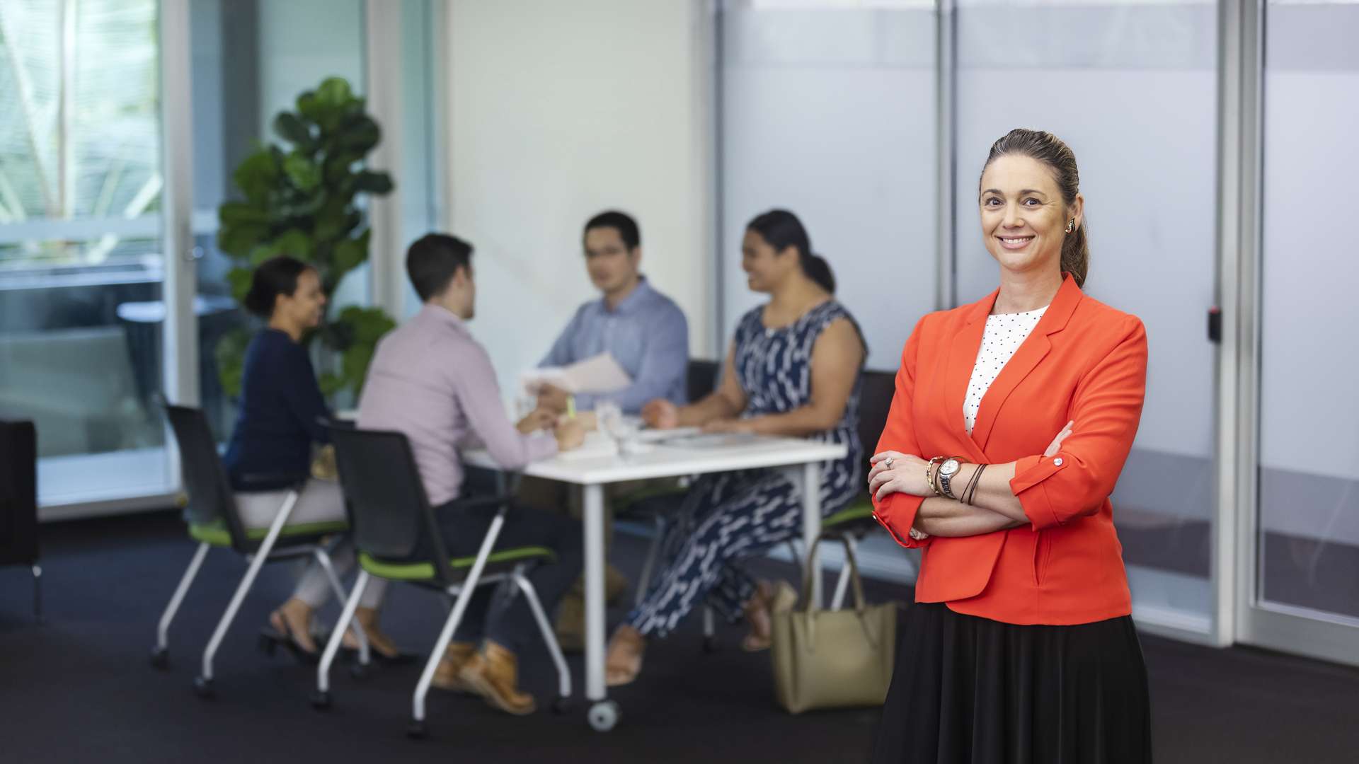 A business student standing in front of the camera, four other students are sitting down working together in the background.