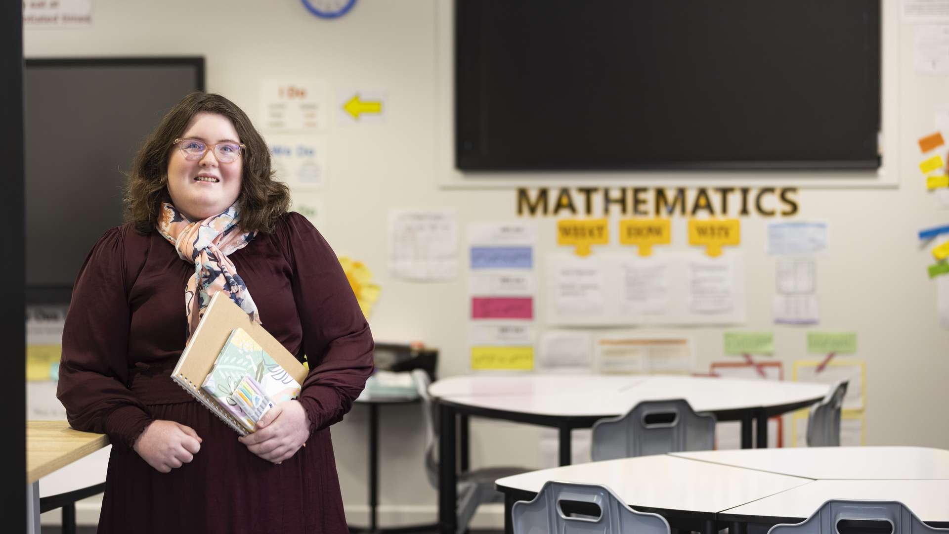 A teaching student standing in a classroom holding two workbooks.