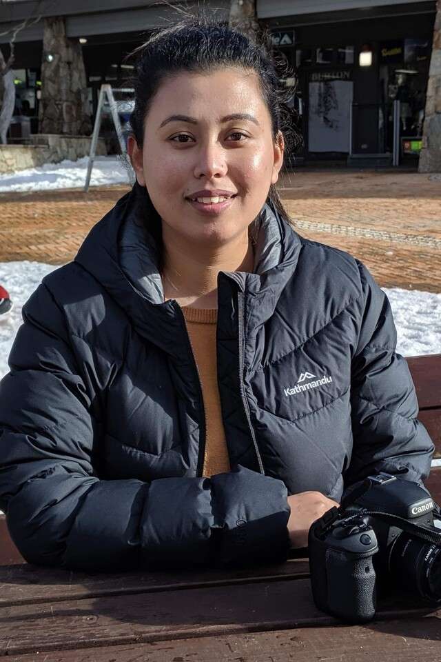 Anita Thapa smiling in a snowy outside area with a camera on the table in front of her