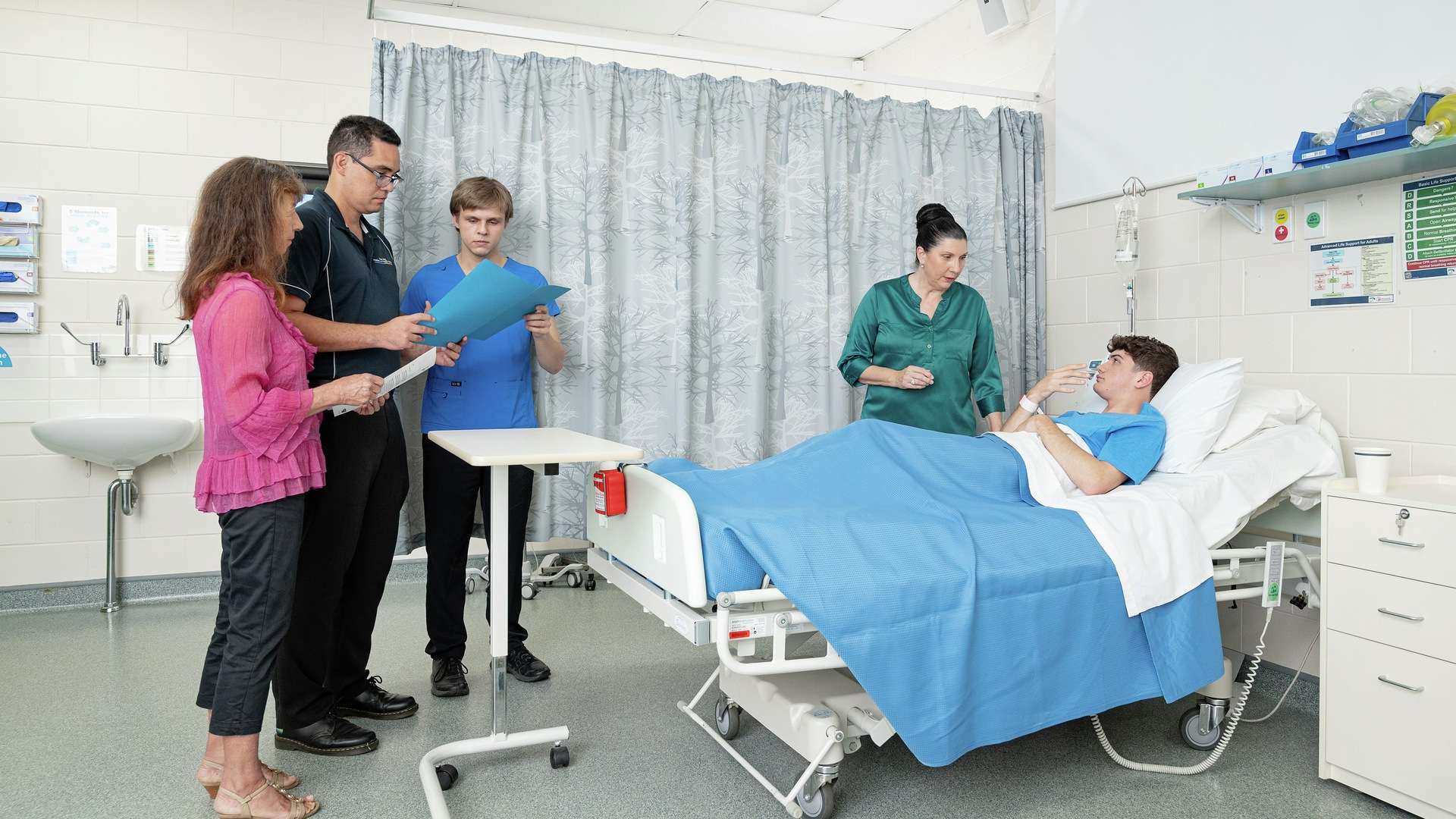 Nursing students and tutors at the bedside of a patient in a hospital ward