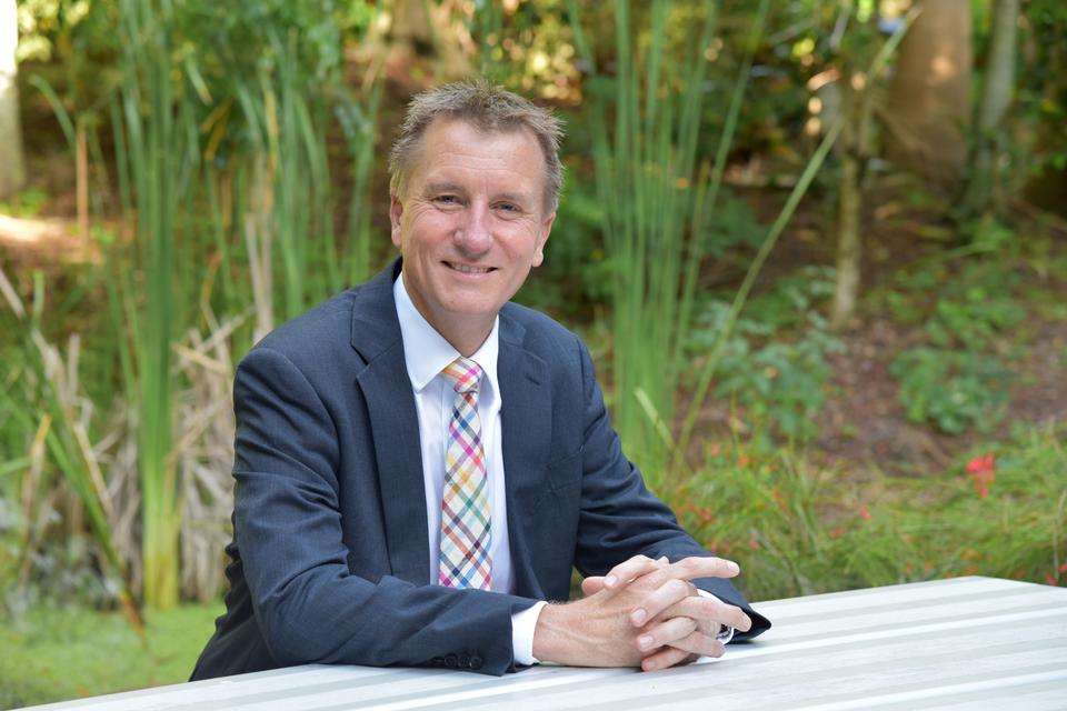 Professor Nick Klomp sitting at a table outside with greenery behind.