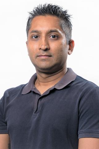 Dr Shaneel Chandra stands in front of a white wall.