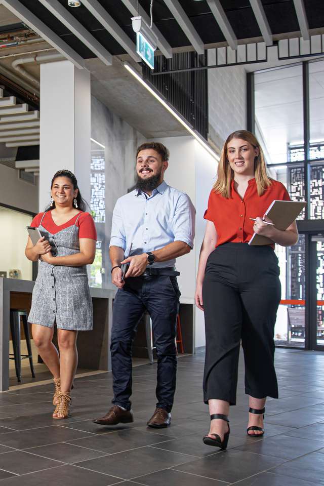 Three students walking through modern building with notepads