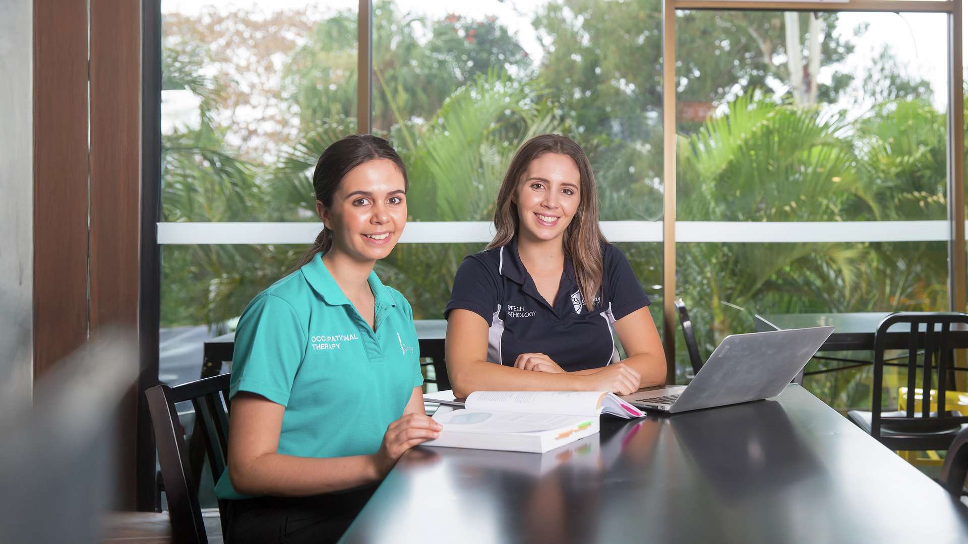Two CQUniCares scholarship students studying with a textbook and laptop