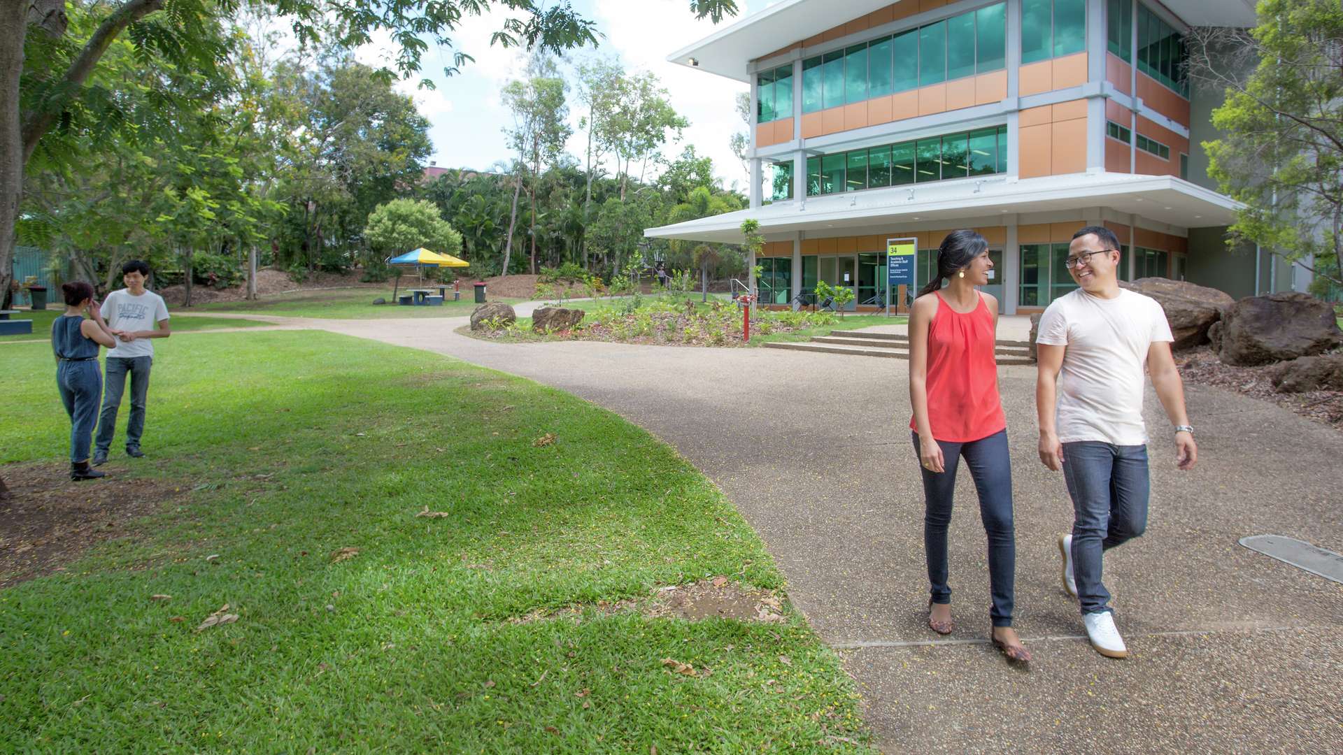Two students chatting and walking along a landscaped path outside Rockhampton campus
