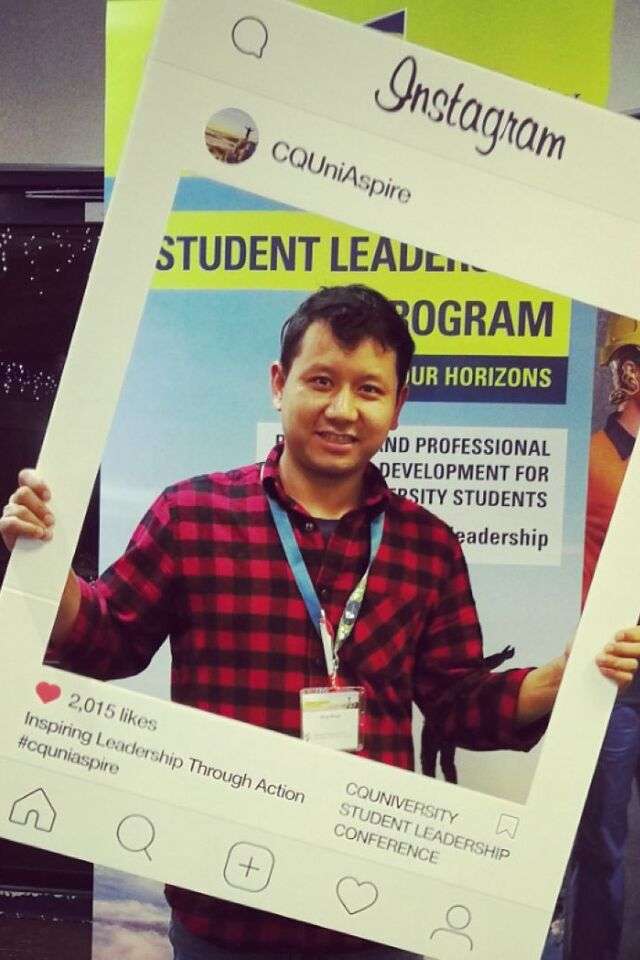 Niraj Thapa Magar holding CQU Student Leadership conference Instagram sign in front Student Leadership Program pull up banner