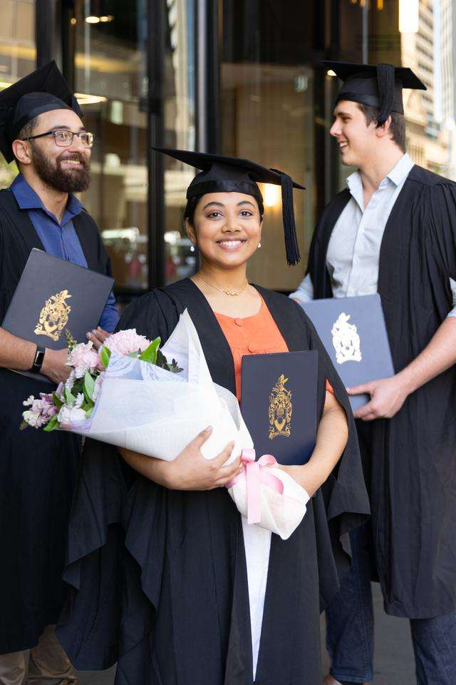 Graduate in regalia at Brisbane campus with two peers