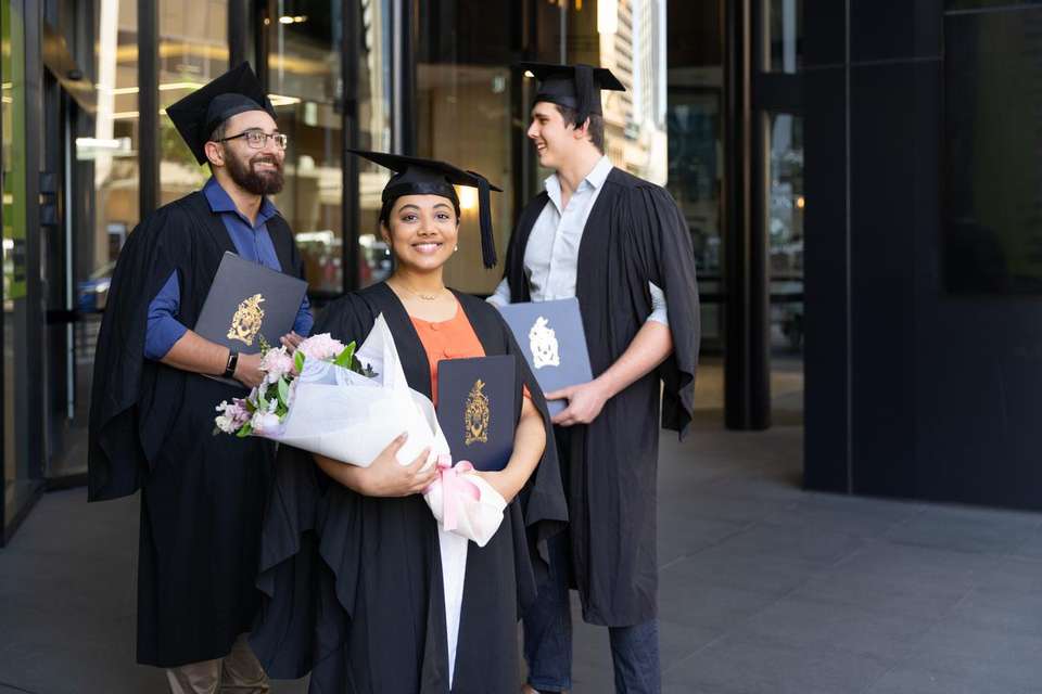 Graduate in regalia at Brisbane campus with two peers