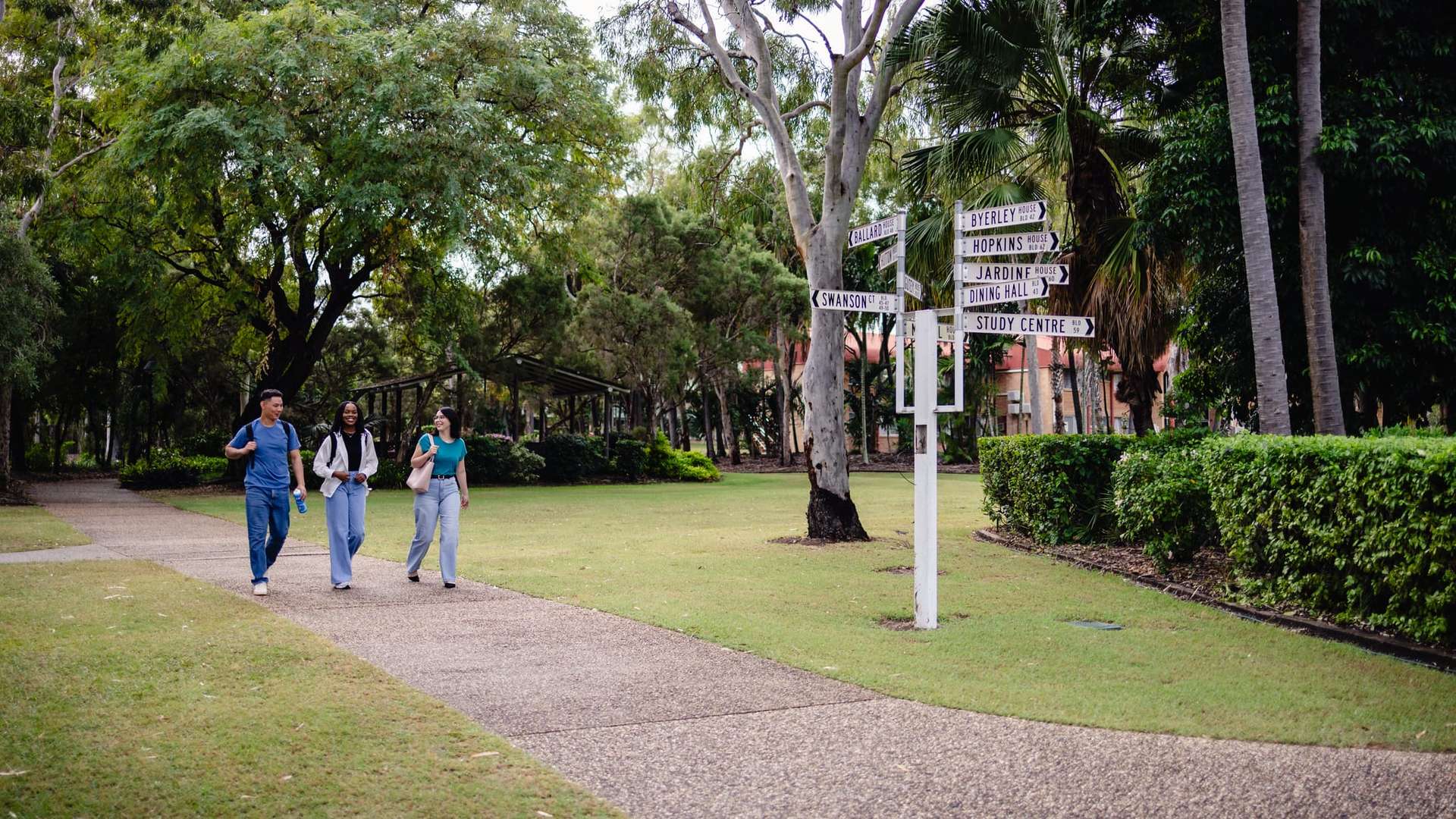 A group of three people walk along a paved path in a leafy park.