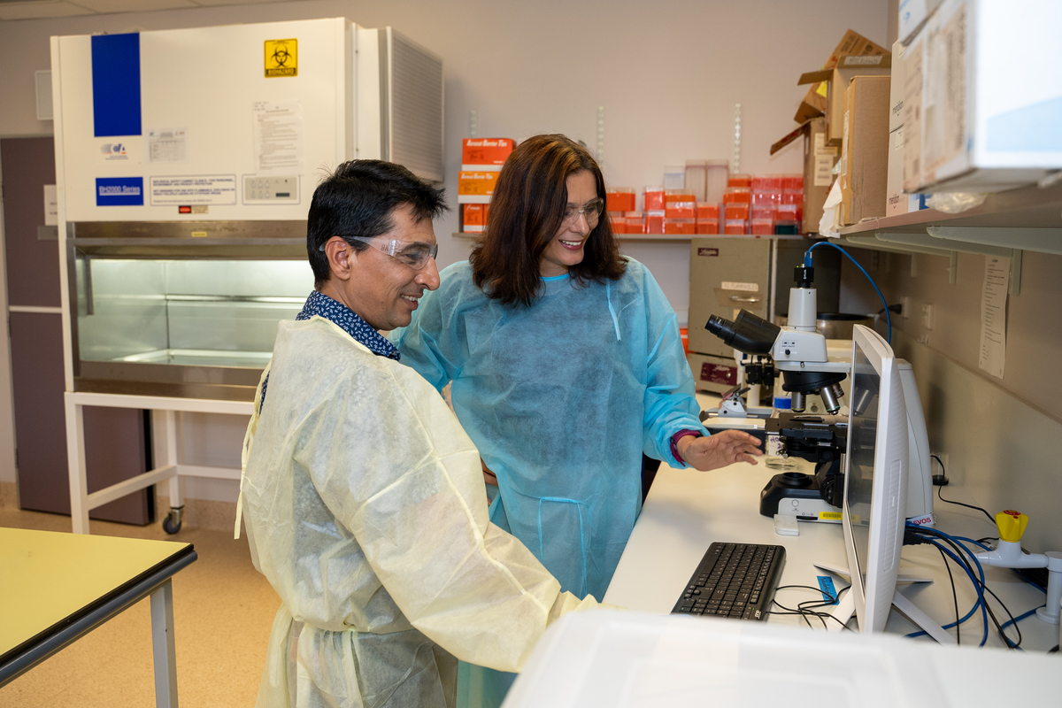 Two researchers review results on a computer in the lab while wearing protective clothing and safety glasses.