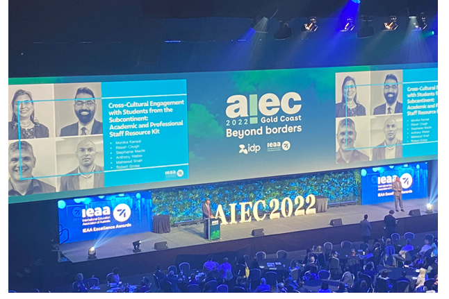 AIEC Gold Coast 2022 Awards Stage with CQU staff memebers pictures on the screen taken from a stadium seat