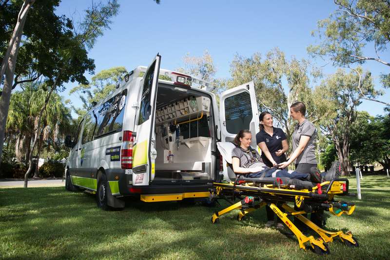 Two paramedic students practice using a stretcher while being guided by a lecturer