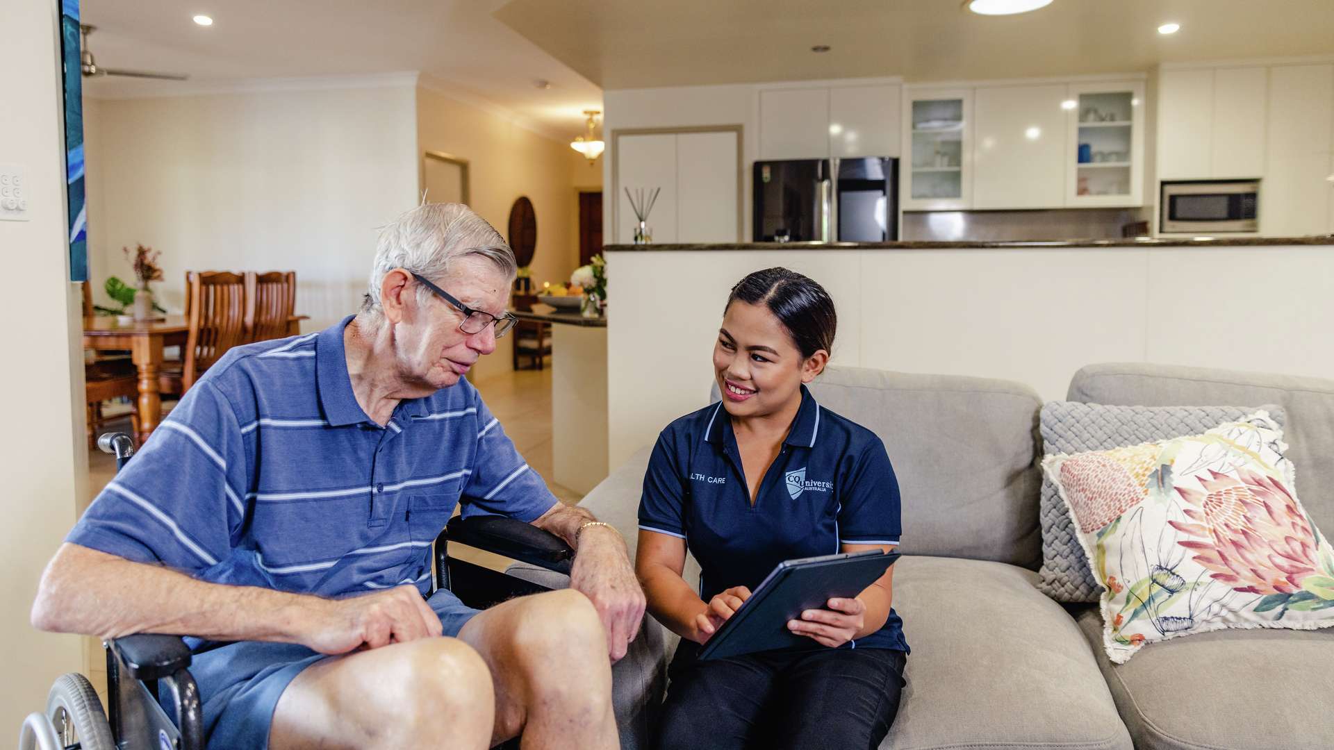 A CQU student assists an older gentlemen who is in a wheelchair as part of a home care service.