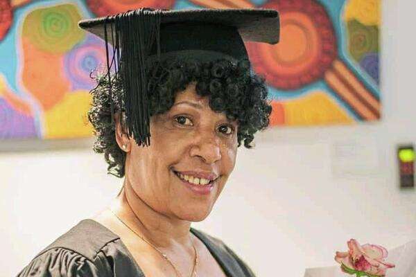 International student Anna Klawe from PNG wearing graduation regalia and holding a flower.