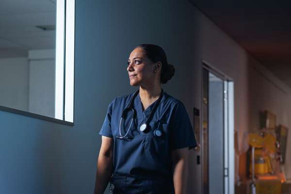 Nursing student standing in a hospital hallway smiling out a window