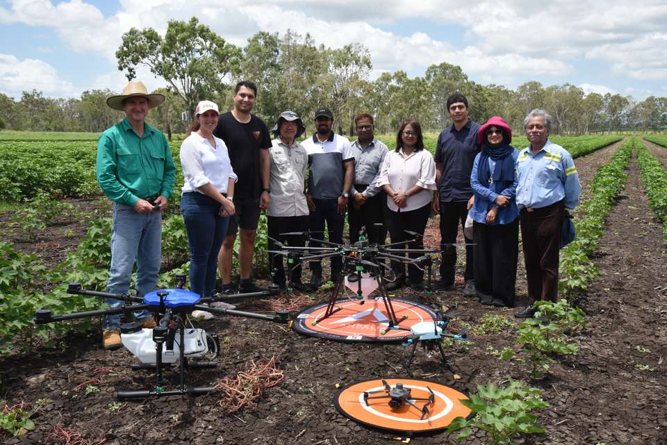 CQUniversity and Foxwell Farms represenatives stand in a cotton field, in front of three drones.