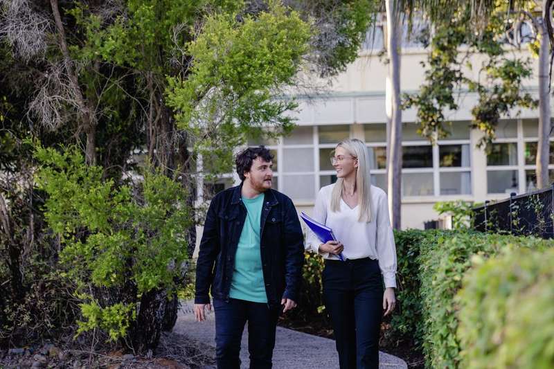 Two students walking to class along a Rockhampton Campus path surrounded by trees