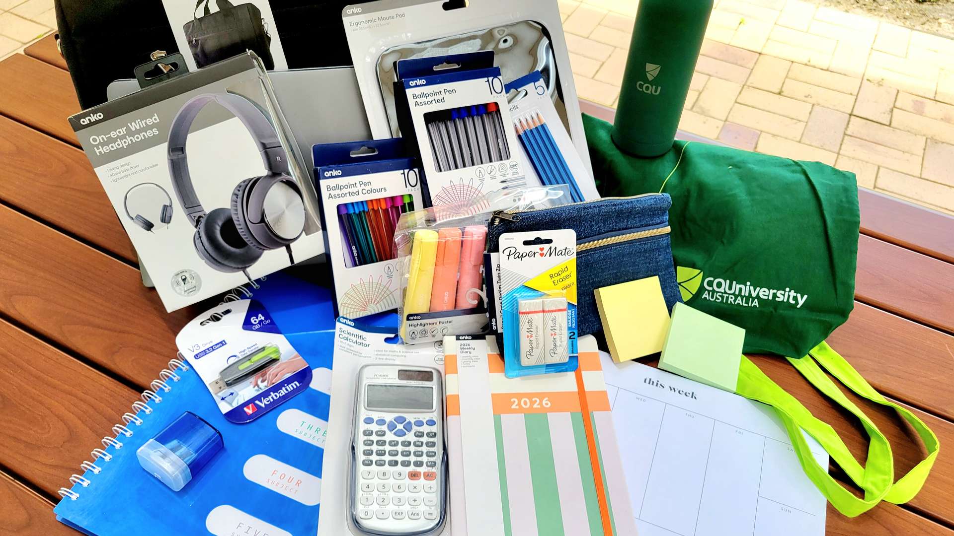 Stationery pack items on a table, including laptop bag, mouse, tote bag, headphones, calculator, pens, pencils, and notepads.