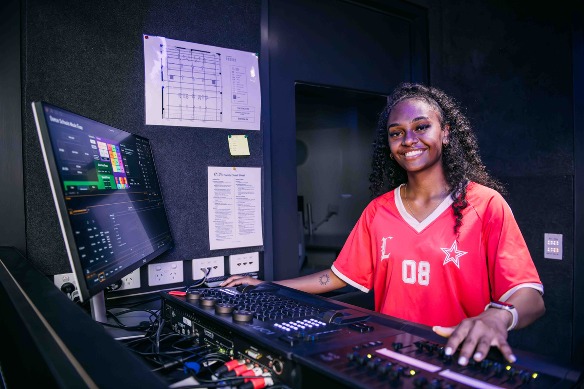 Binalmalmal student sitting at a theatre technical equipment desk smiling at the camera