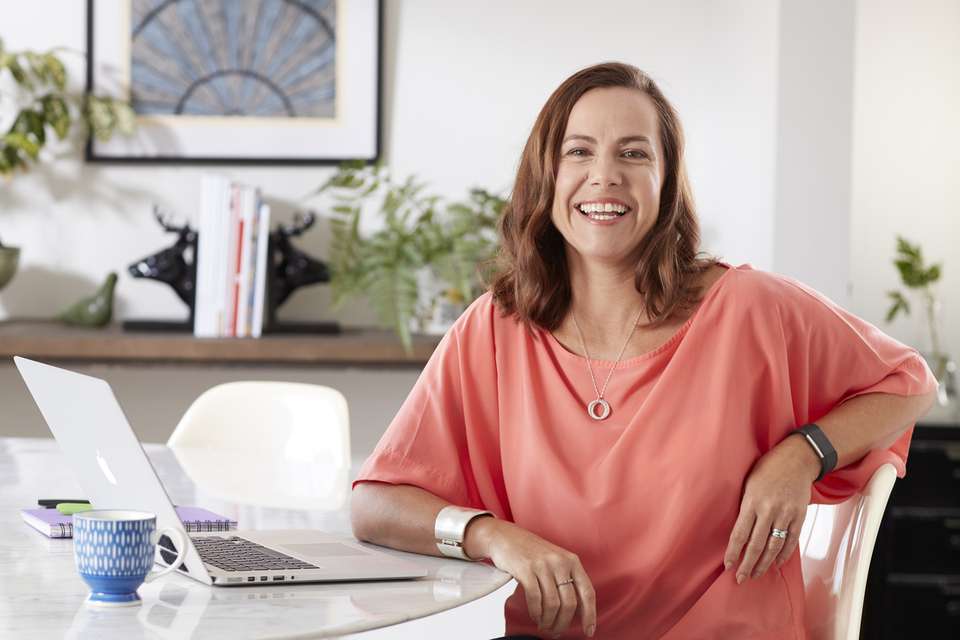 Person smiling at camera and sitting at white table with laptop studying.