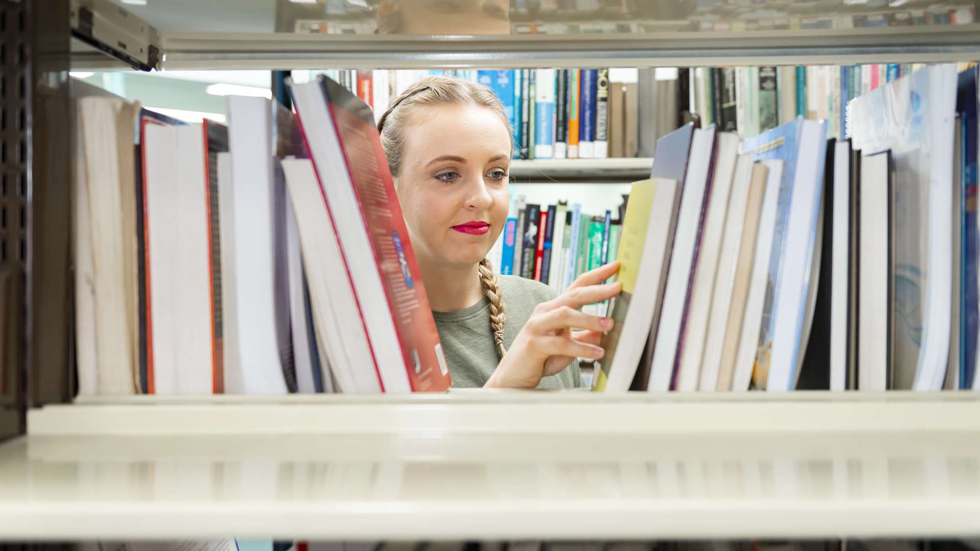A student looking through textbooks on a shelf in a CQUniversity library