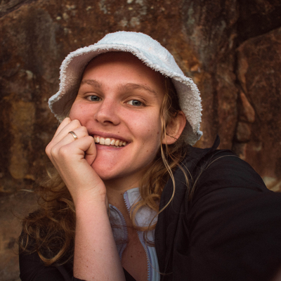 Brandy Bayntun with a white bucket hat, smiling at the camera with her hand resting on the side of her face.