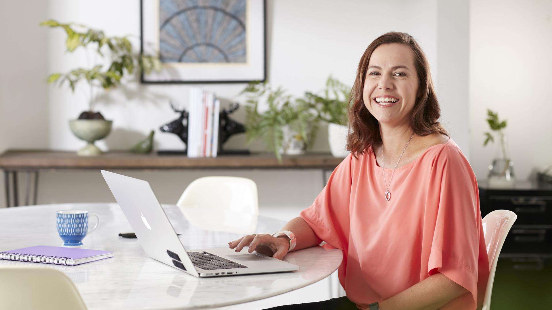 Student smiling at camera with laptop on table.